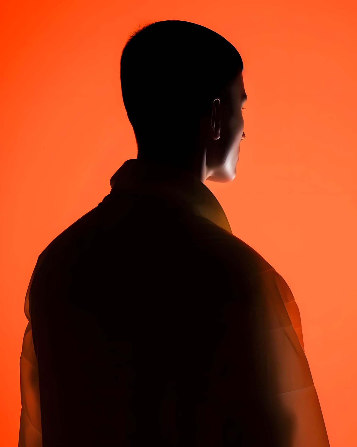 A man seen from behind, silhouetted against an orange wall